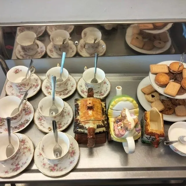 A tray holding many cups and saucers with fine china and a selection of biscuits